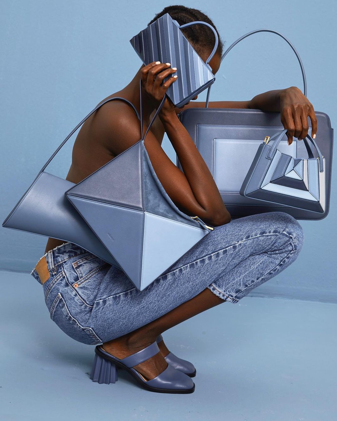 A woman crouches while holding multiple blue handbags