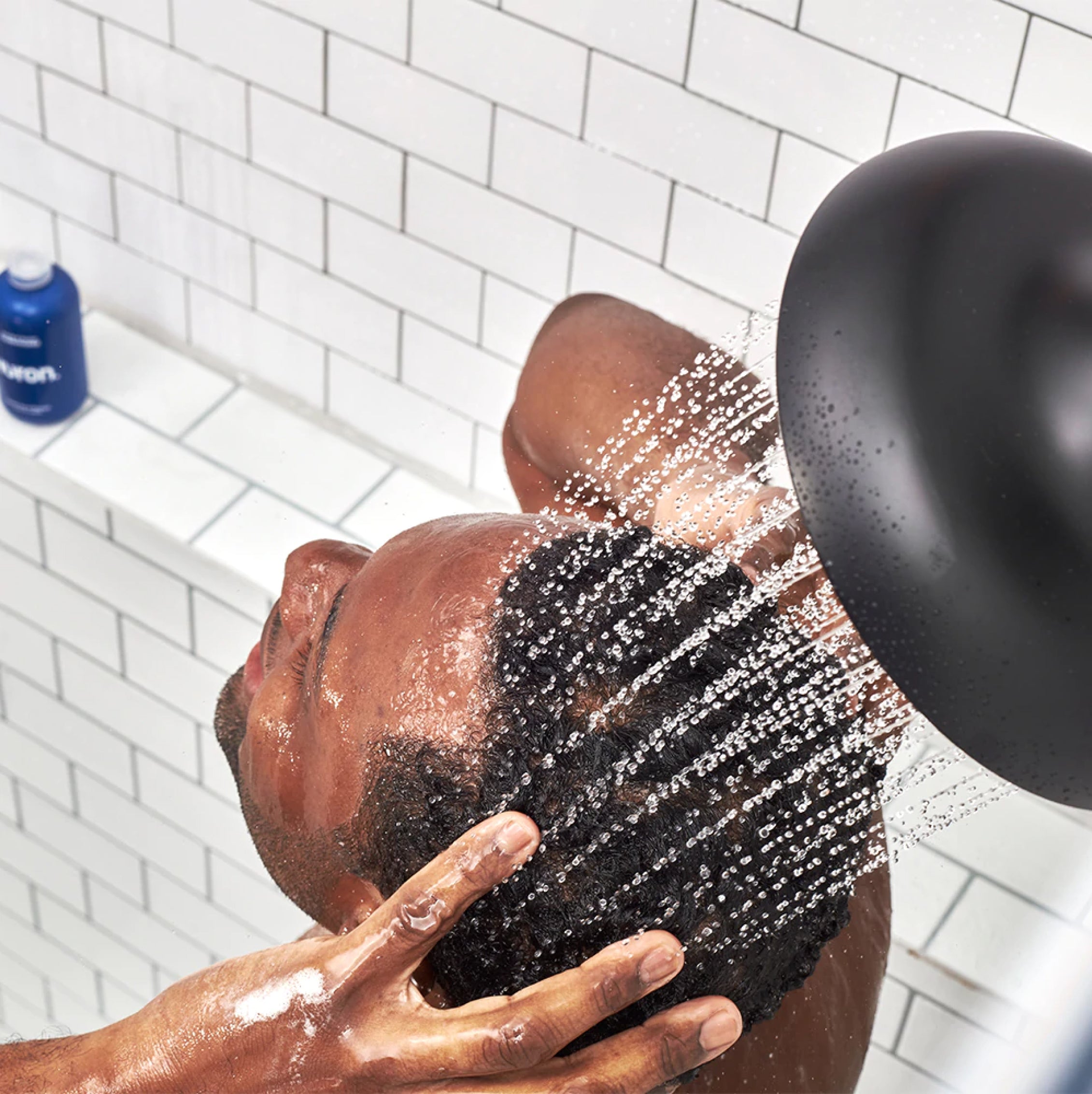 A top-down view of a man washing his hair in a white tiled shower.