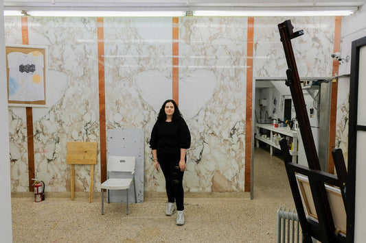 Adria stands in her studio, with art supplies surrounding her. 